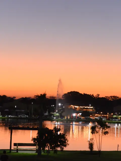 Pôr do sol alaranjado no lago com fonte iluminada